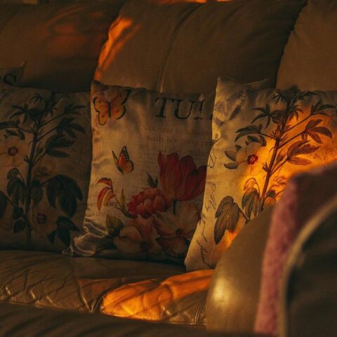 Coussins floraux sur canapé, lumière tamisée, personne assise