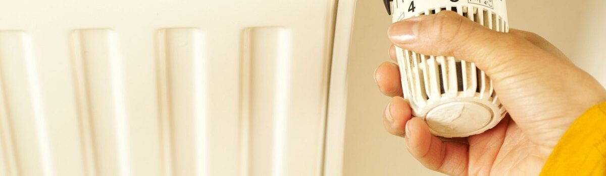 Une main ajuste le thermostat d'un radiateur blanc sur le mur