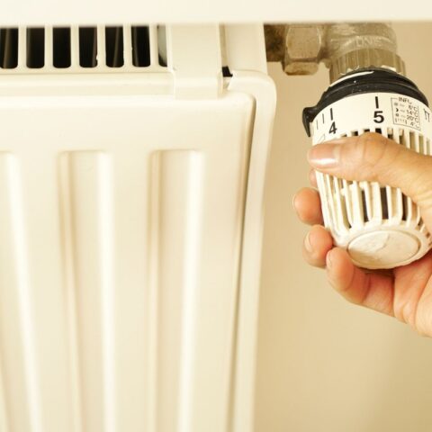 Une main ajuste le thermostat d'un radiateur blanc sur le mur