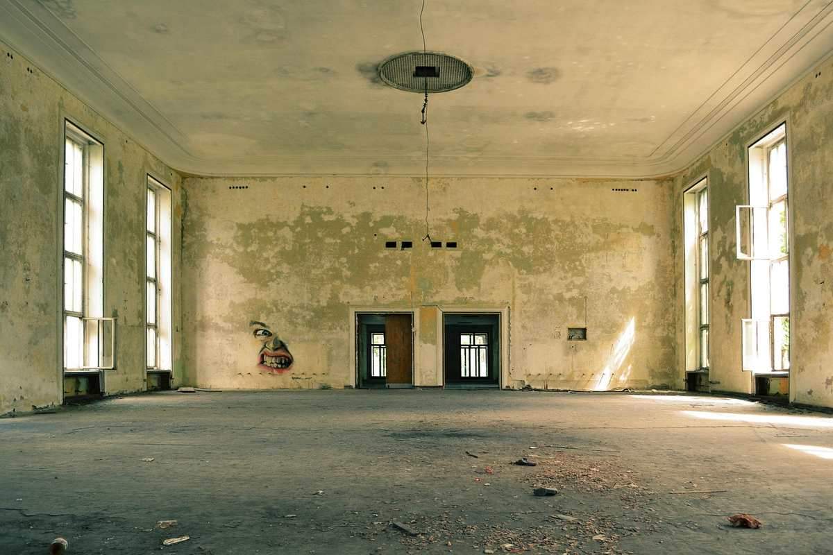 Salle abandonnée avec murs tachés, deux portes et hautes fenêtres