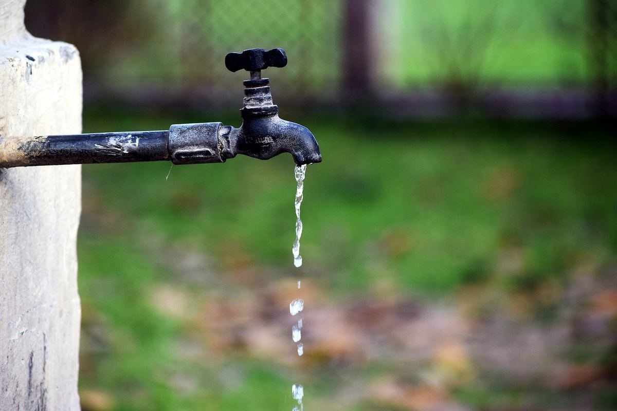 Robinet noir gouttant de l'eau, monté sur un mur blanc avec végétation floue en arrière-plan