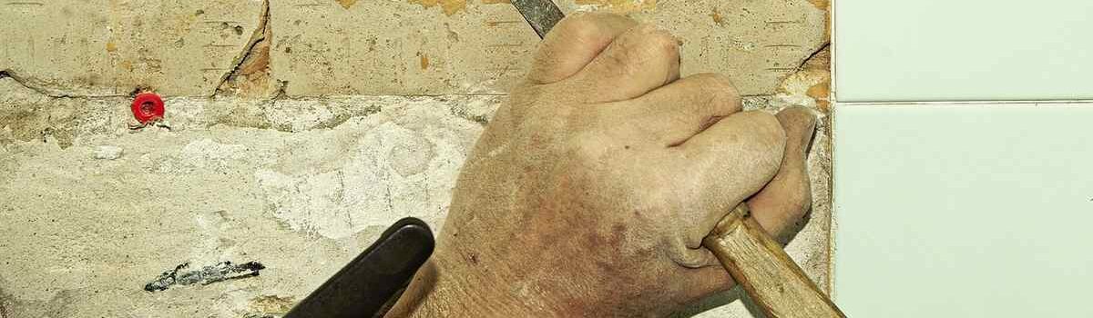 Une main utilise un marteau et un burin pour enlever une tuile