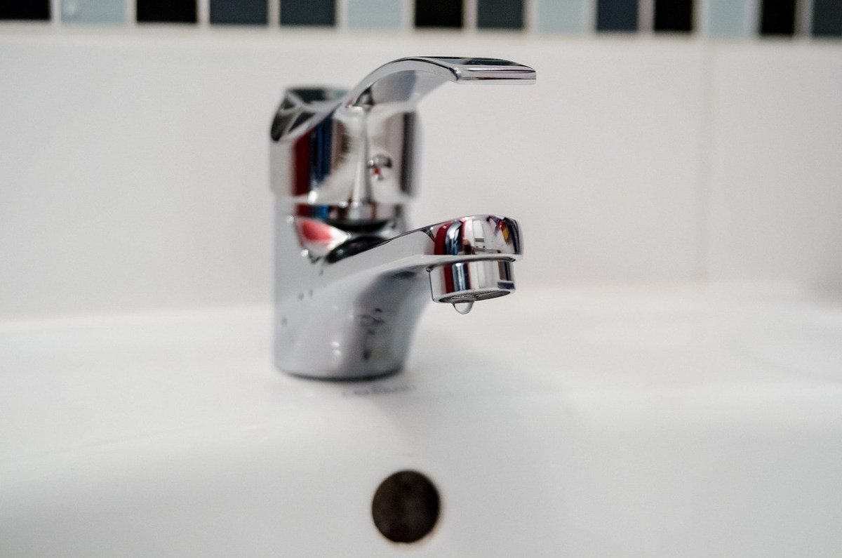 Robinet d'évier en chrome avec goutte d'eau, carrelage blanc, trou d'écoulement