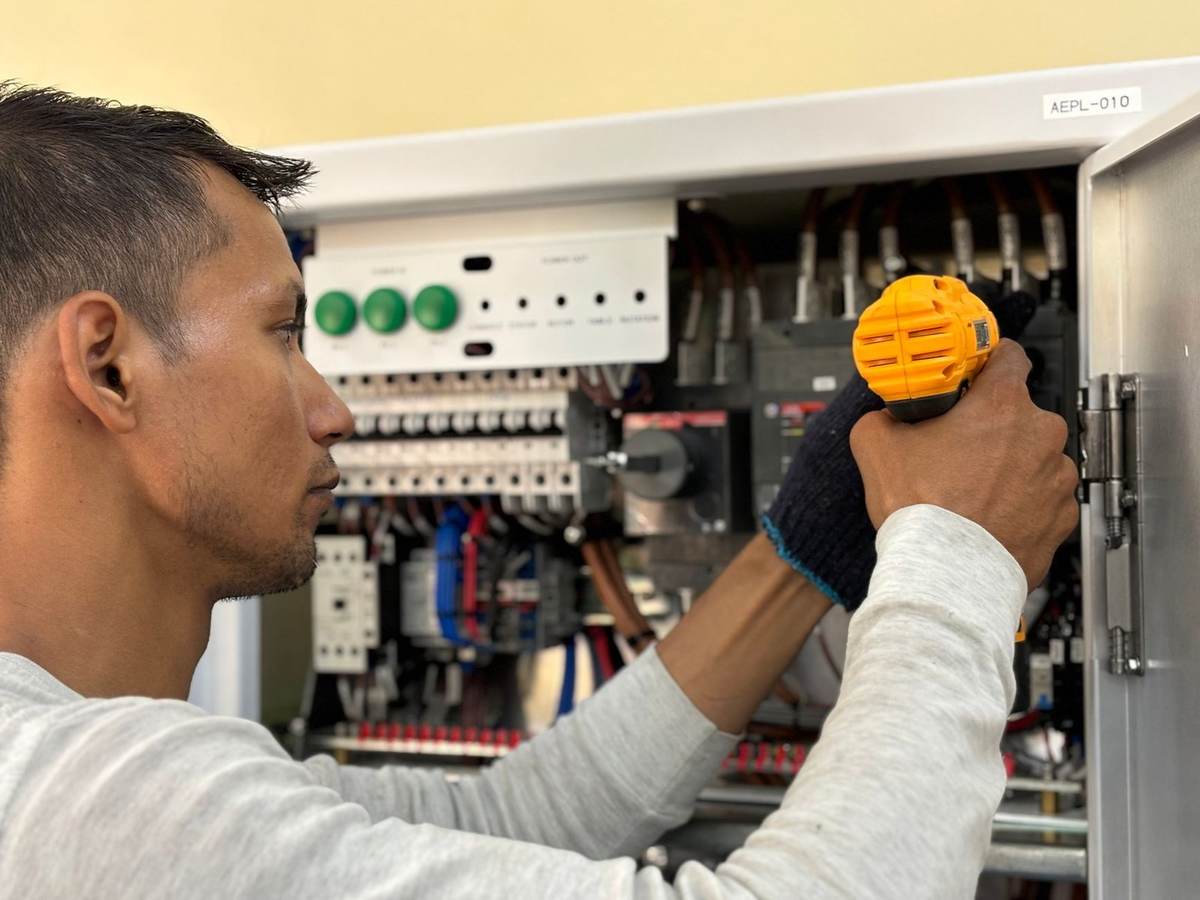 Homme manipulant un tournevis jaune sur un tableau électrique ouvert