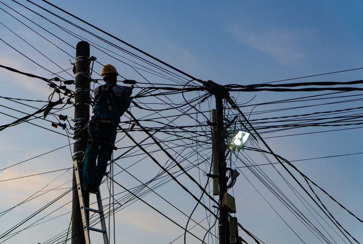Ouvrier sur échelle près de poteau électrique, câbles enchevêtrés, ciel clair