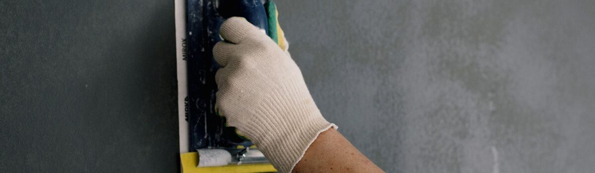 main gantée applique de la pâte noire sur un mur gris
