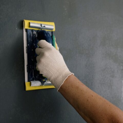 main gantée applique de la pâte noire sur un mur gris
