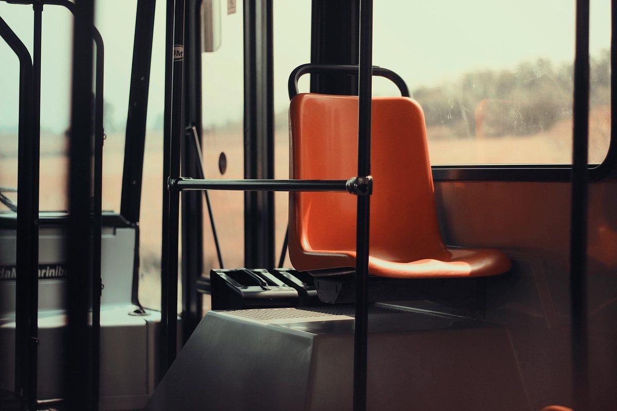 Intérieur d'un bus avec siège orange, barres, fenêtres et paysage flou