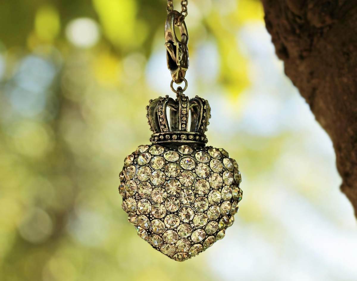 Pendentie en forme de coeur avec couronne, suspendue a un arbre, contre un fond flou de feuillage Pendentie en forme de coeur avec couronne, suspendue a un arbre, contre un fond flou de feuillage
