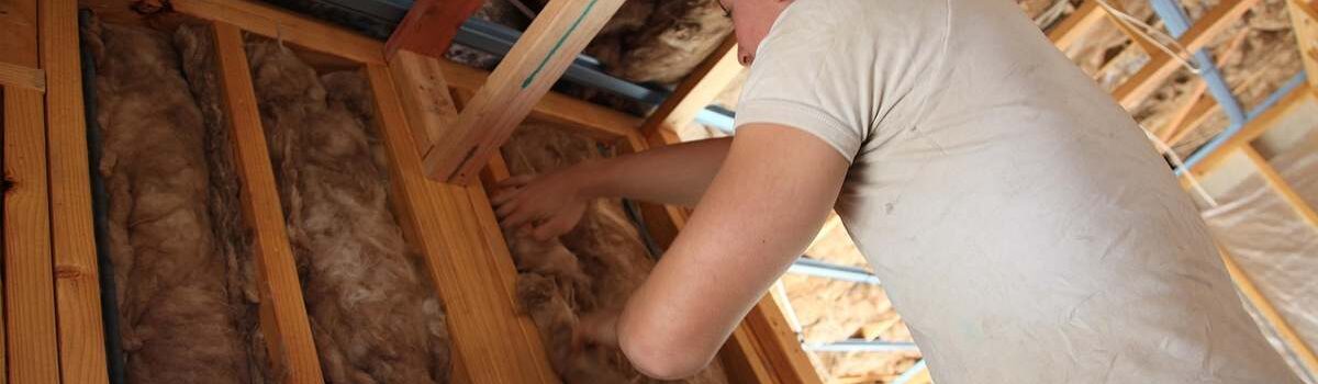 Un homme installe de la laine de verre entre les solives